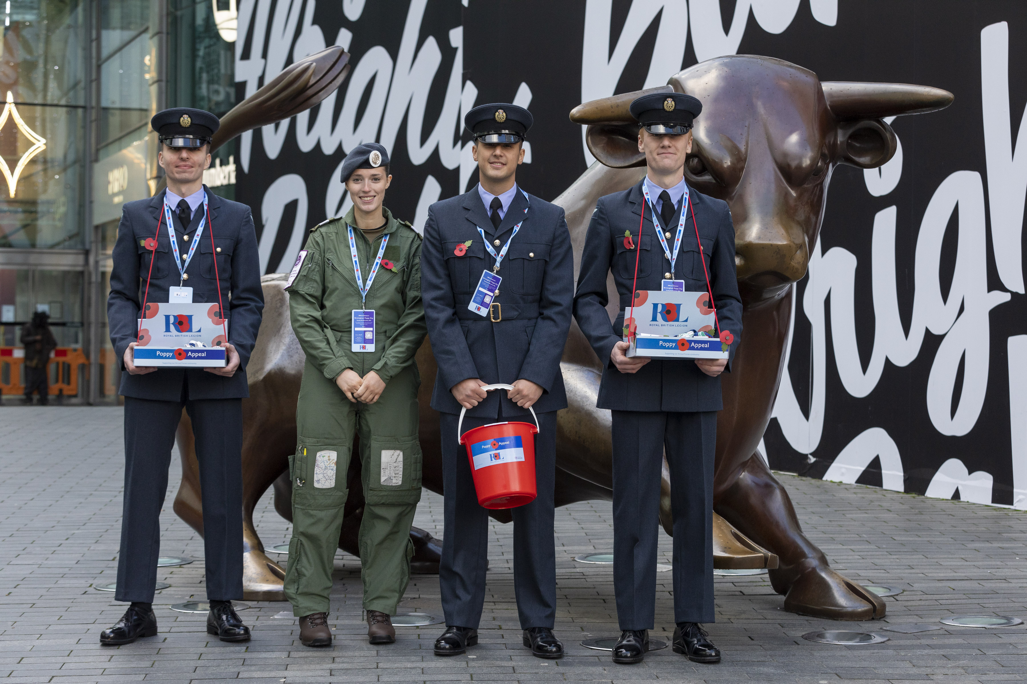 Image shows RAF aviators holding poppy collection boxes, by statue of bull in Birmingham.